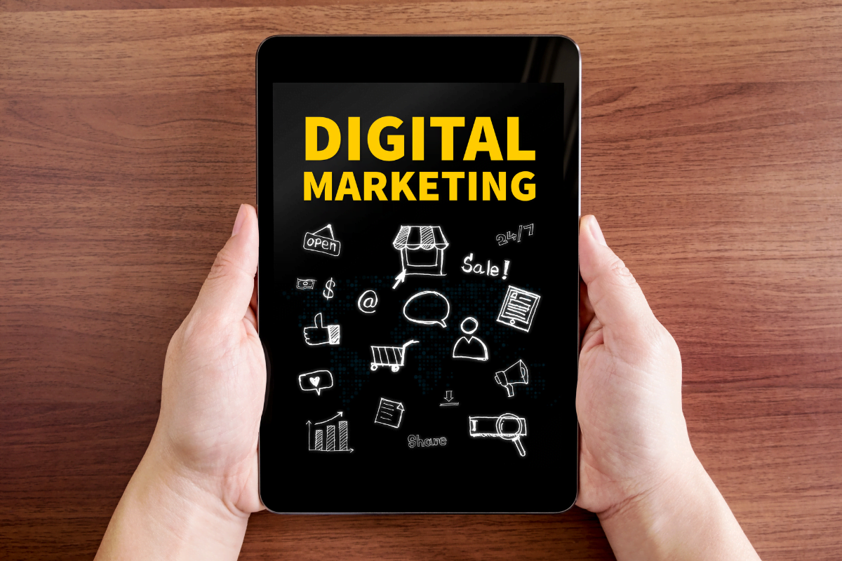 A hand holding a tablet displaying the words "digital marketing".