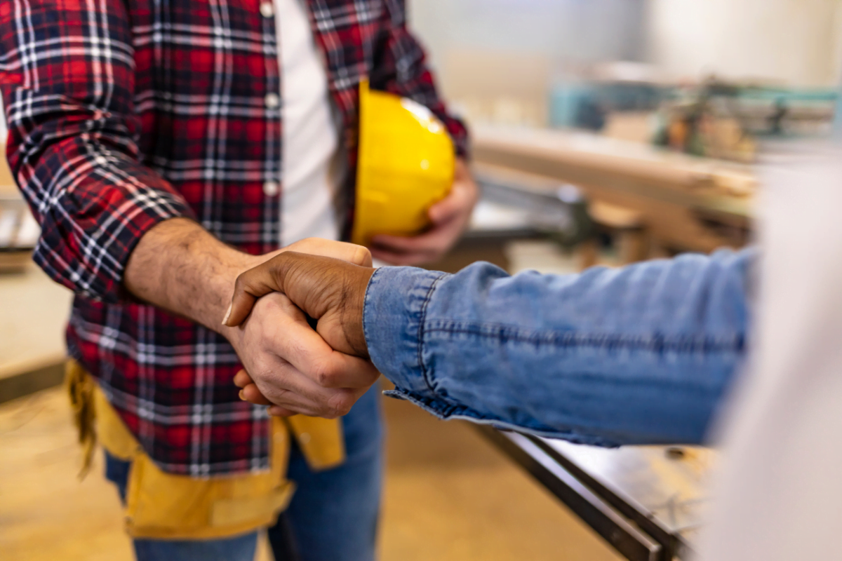 Two construction workers shaking hands in a factory, showcasing the trust and professionalism essential for successful collaborations between contractors.