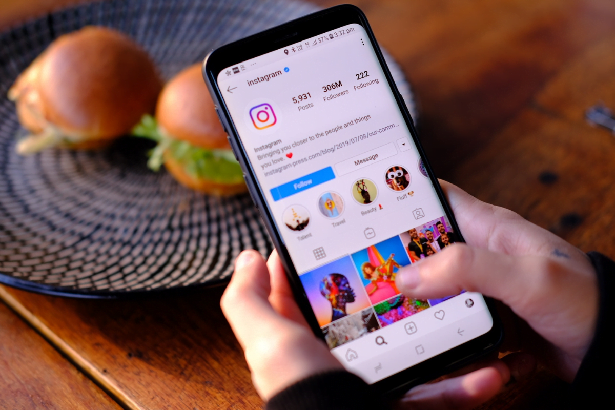 An individual showcasing their Instagram marketing strategy by holding an phone while posing with a delectable plate of food.