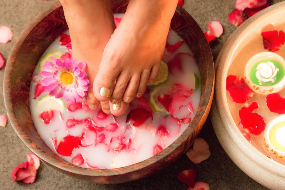 A woman's feet immersed in a bowl of refreshing water adorned with delicate flowers and surrounded by soothing candles, creating a blissful ambiance perfect for an indulgent spa retreat.