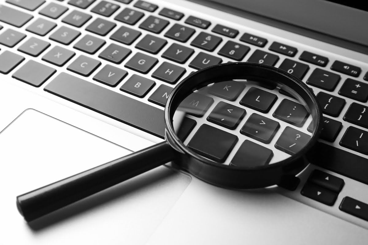 A magnifying glass delicately placed on top of a laptop keyboard, showcasing an intense focus on conducting a comprehensive website audit checklist.