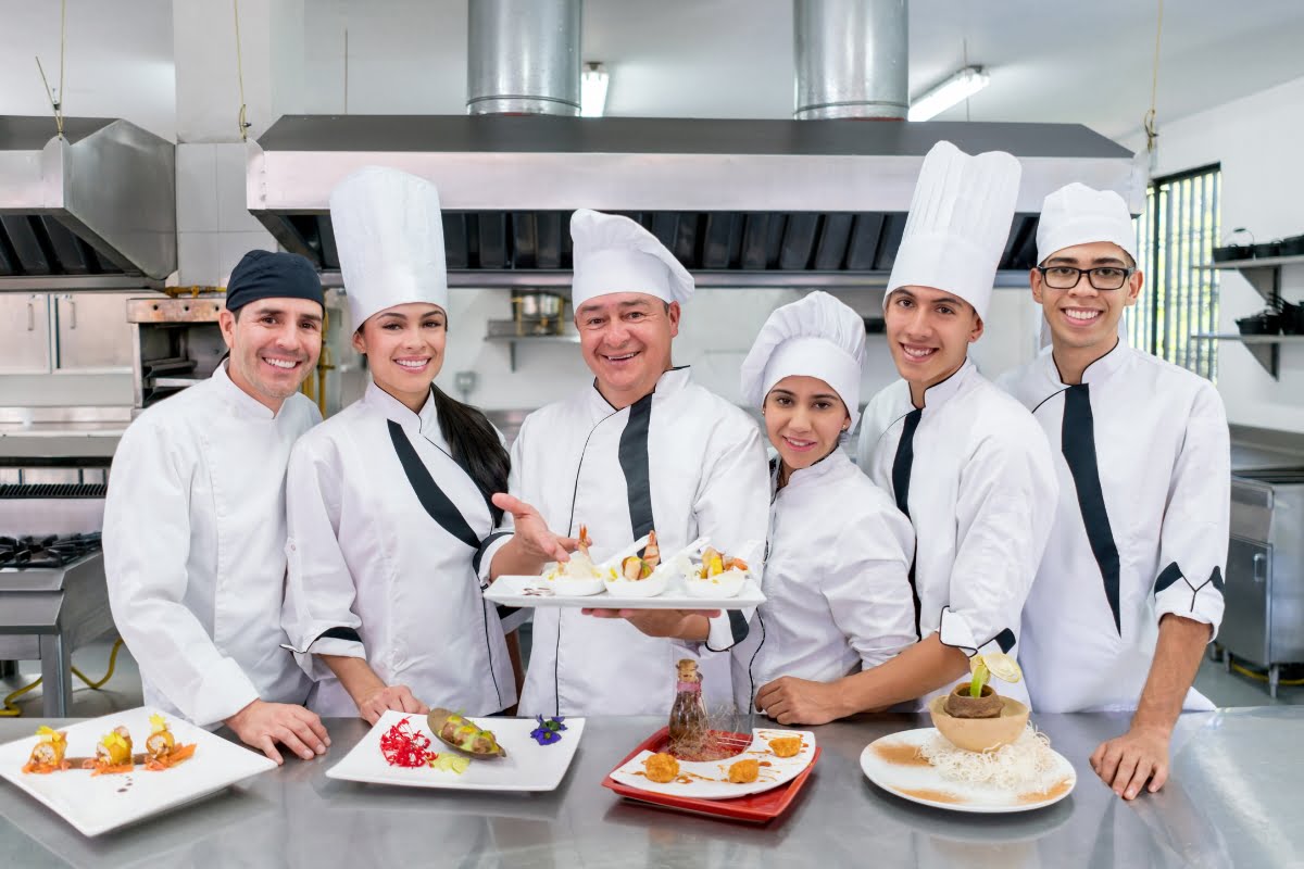 A group of chefs posing for a photo with catering clients in a restaurant.