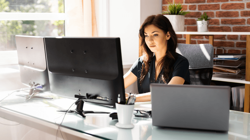 A woman brainstorming content ideas at her desk with two computers.