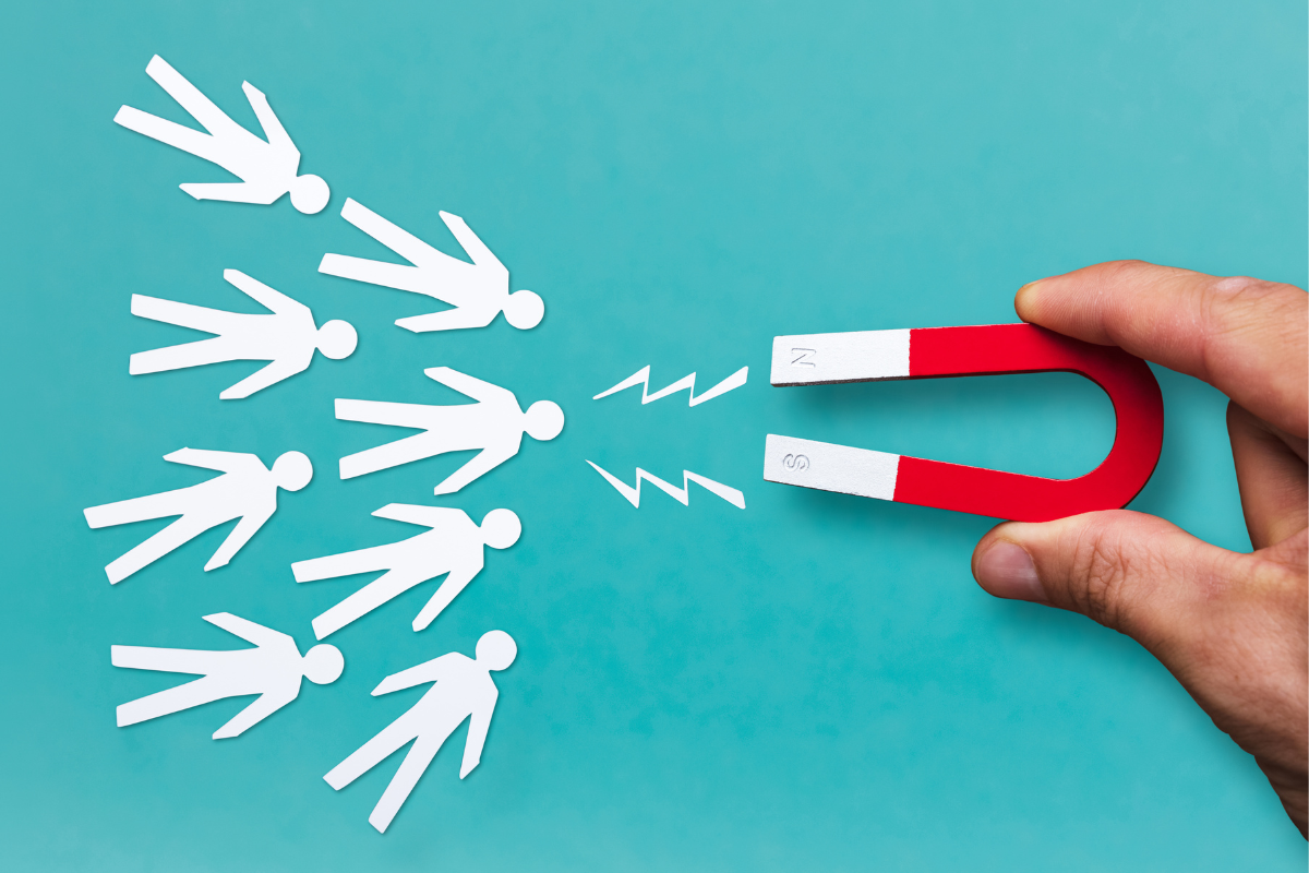 A hand holding a magnet to a group of paper people.