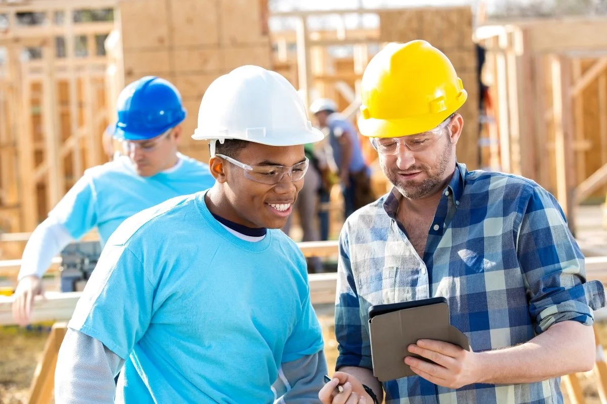 Two home builder construction workers with hard hats looking at a tablet.