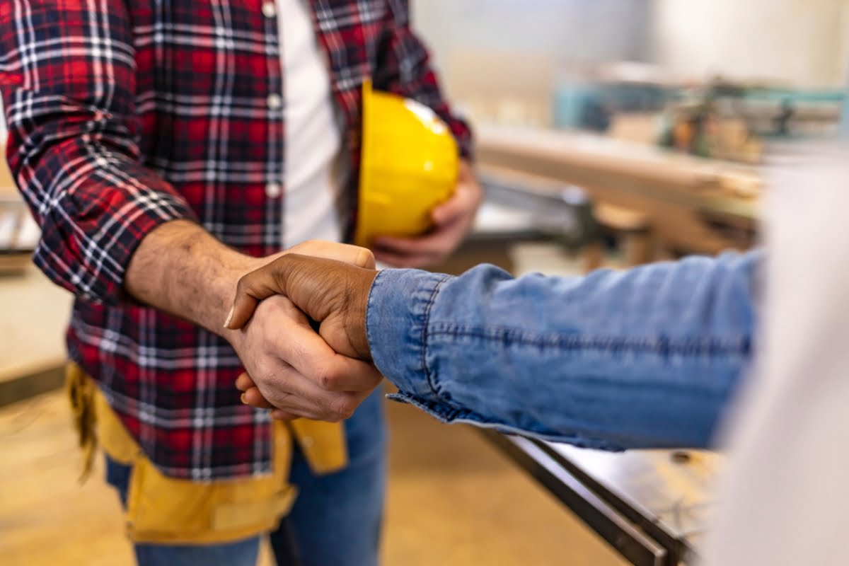 Two construction workers shaking hands in a factory, showcasing their expertise in HVAC services for local businesses.