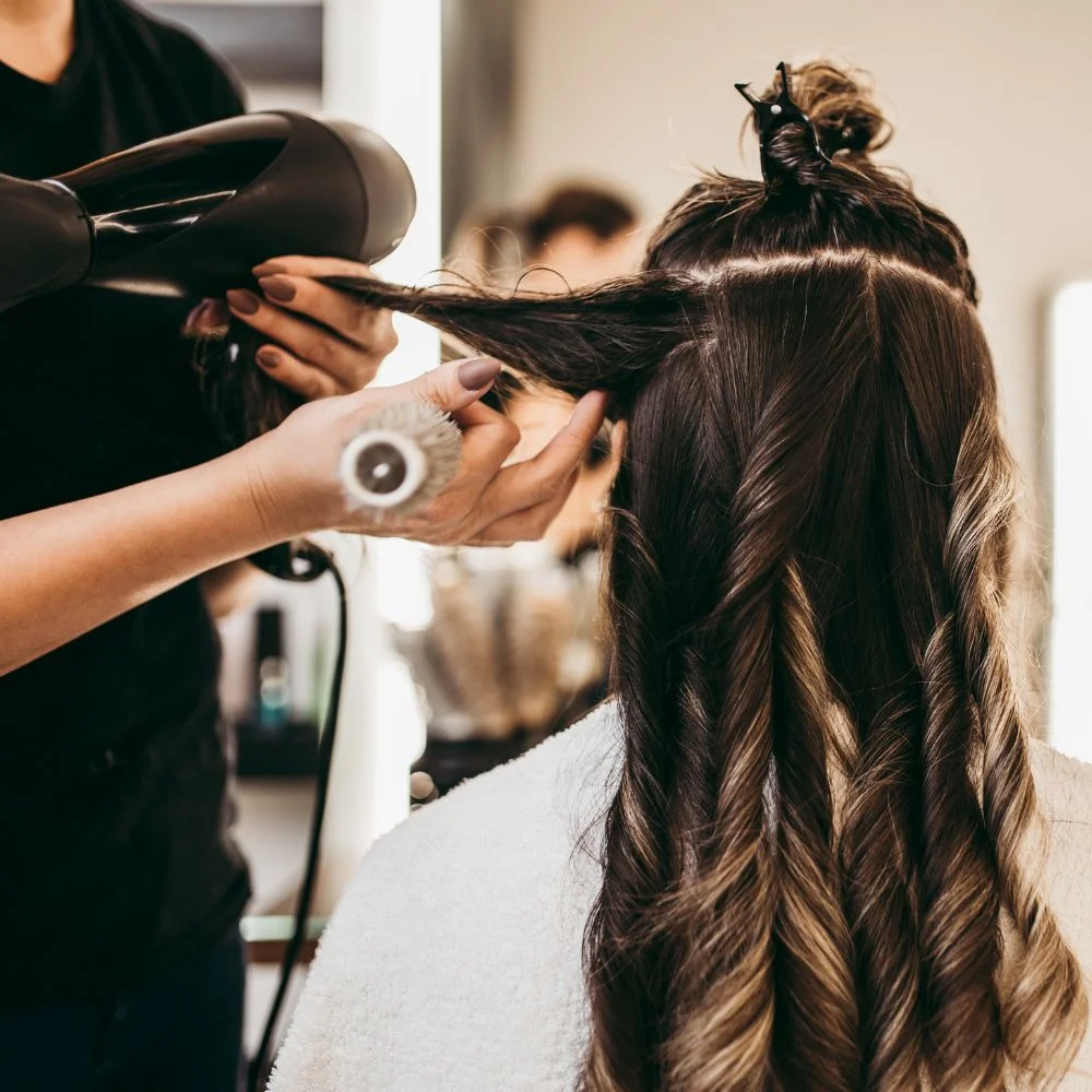 A woman getting her hair done at a salon with the assistance of a hair stylist.