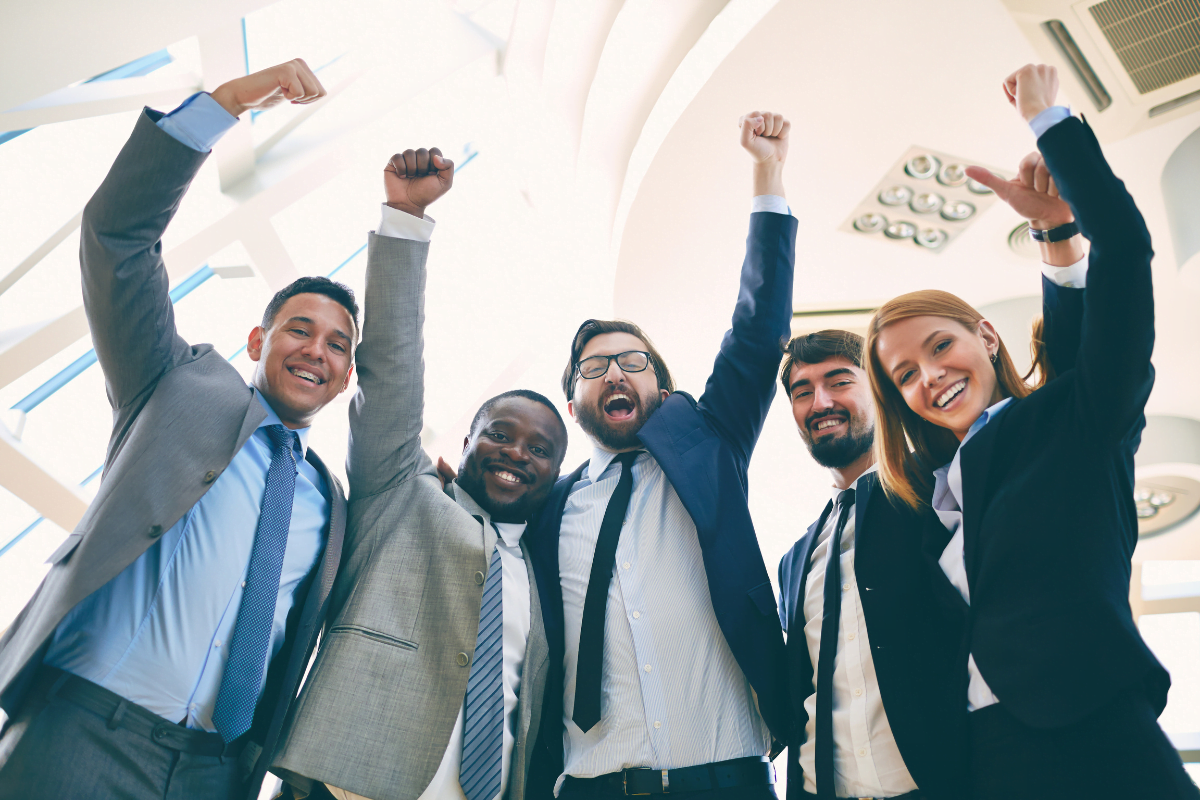 A group of business people celebrating with raised fists in the air.