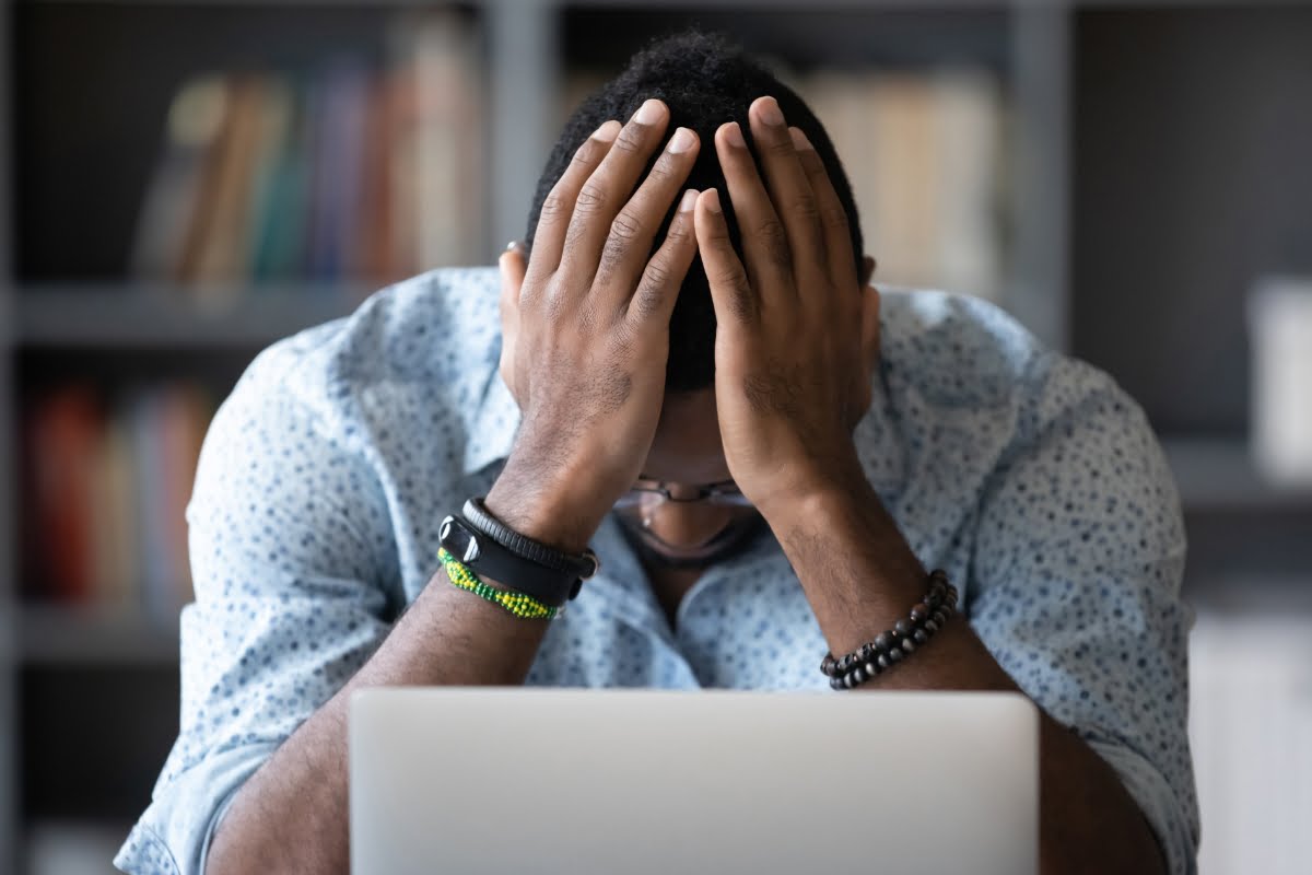 A man with his hands on his head in front of a laptop, seemingly frustrated with low quality content on a website.