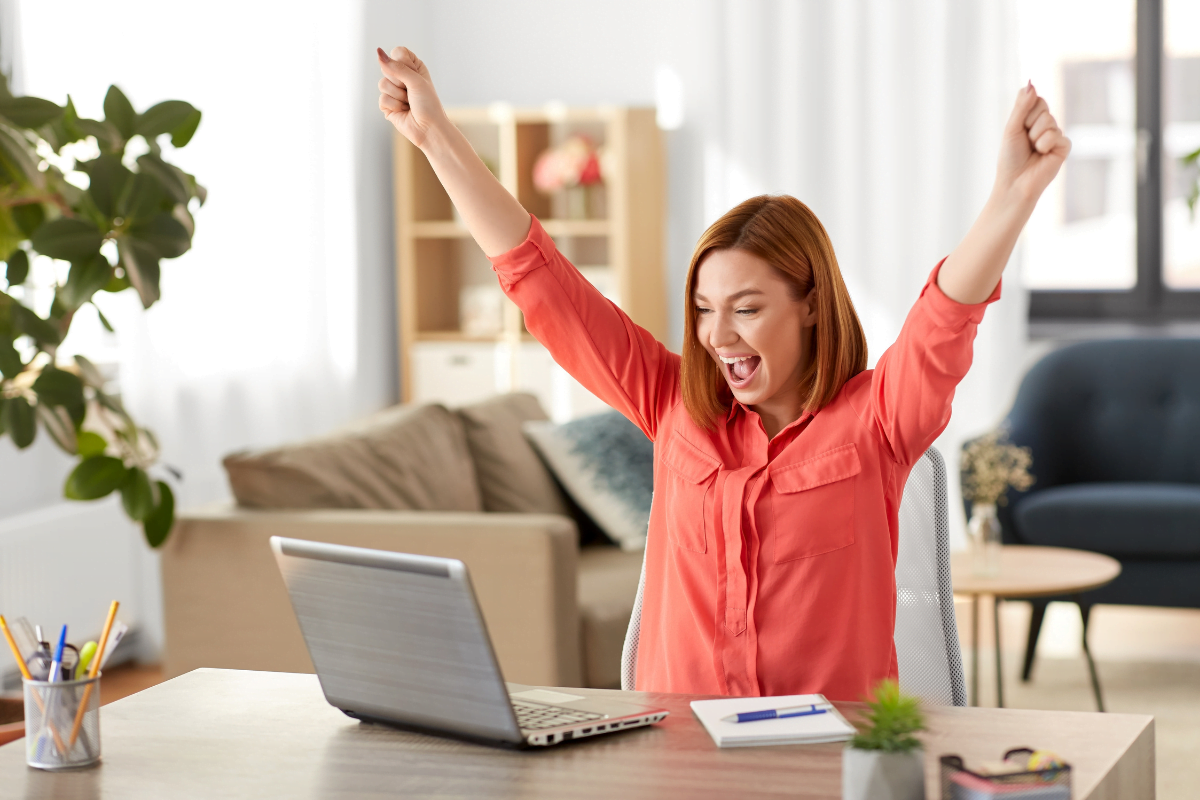 A happy woman is raising her hands while using a laptop due to better search engine ranking.