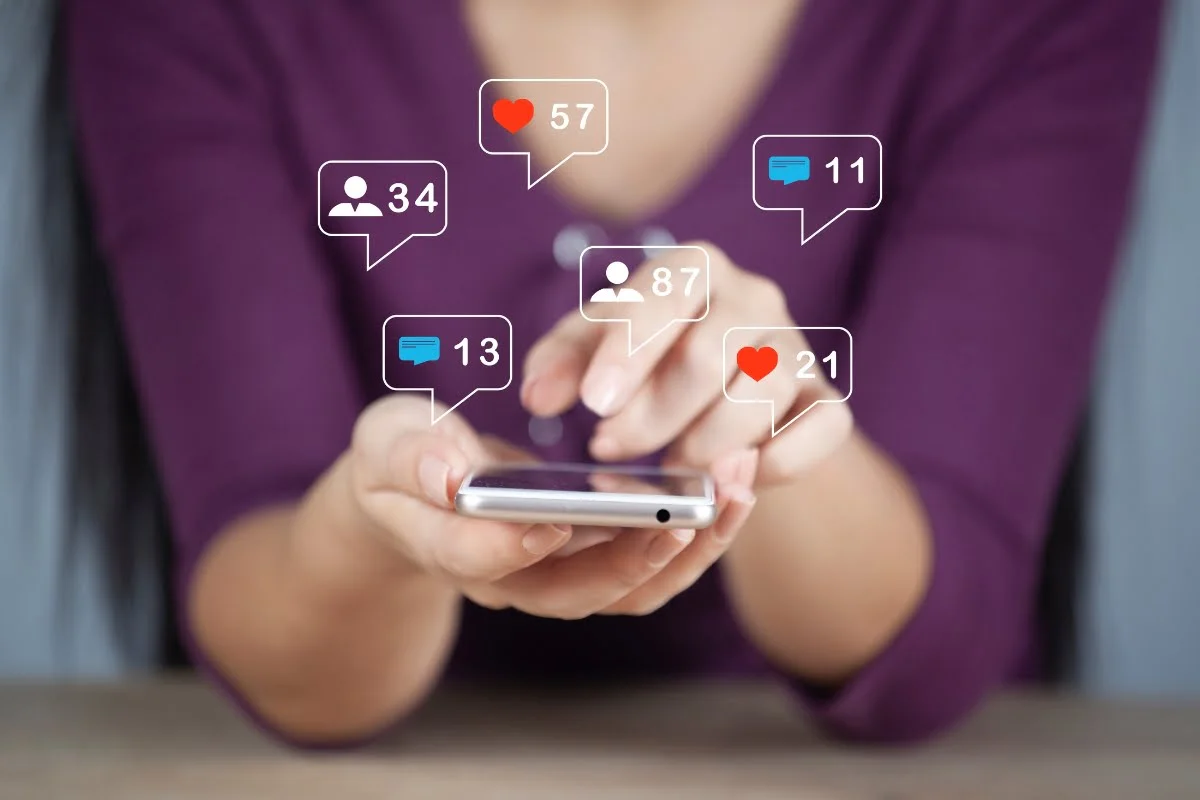 A woman holding a cell phone displaying social icons, unaware of the potential shadow banning.