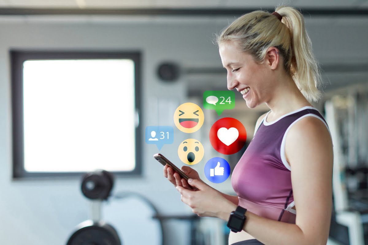 A woman is browsing social media on her smart phone while working out at the gym, showcasing the intersection of technology and fitness.