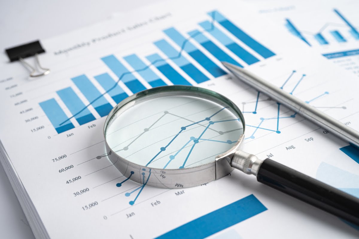 A magnifying glass and pen on a paper with data-driven graphs and charts.