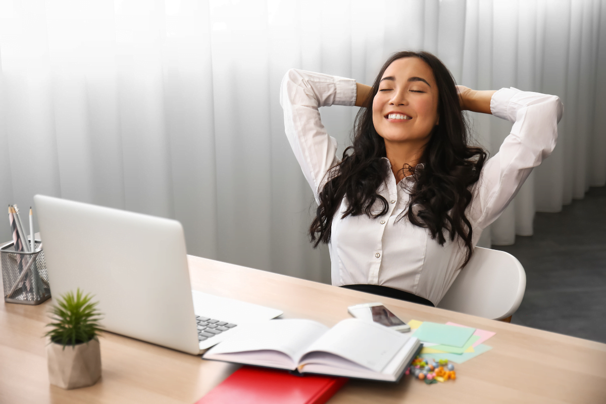 A woman is sitting at a desk with her hands raised while automating her marketing strategies.