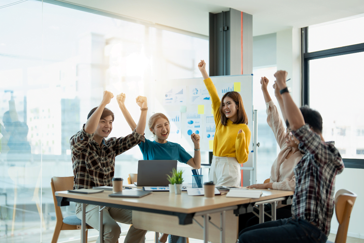 A lively gathering of individuals commemorating at a table in an office, creating an atmosphere of camaraderie and cheer.