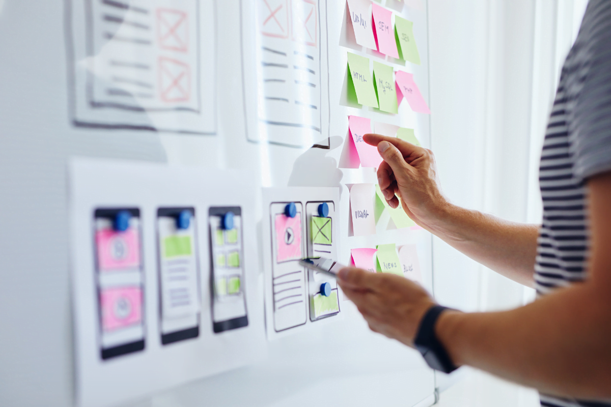 A person is organizing sticky notes on a white board to create a mobile friendly website.