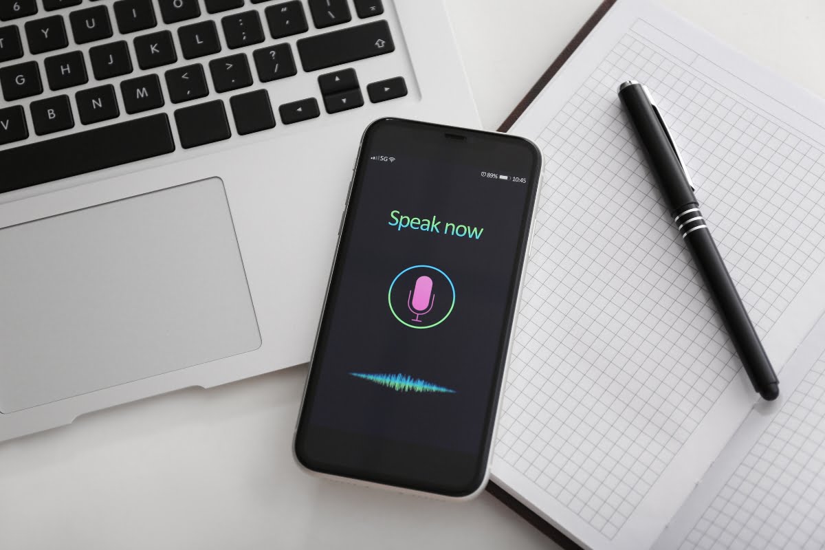 A smartphone with a microphone on it next to a notebook and pen for voice search capability.