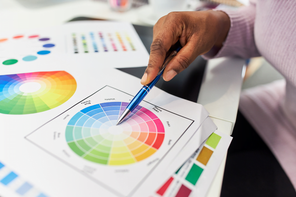 A woman, seated at a desk, holding a color wheel and examining it alongside a pen in her hand.