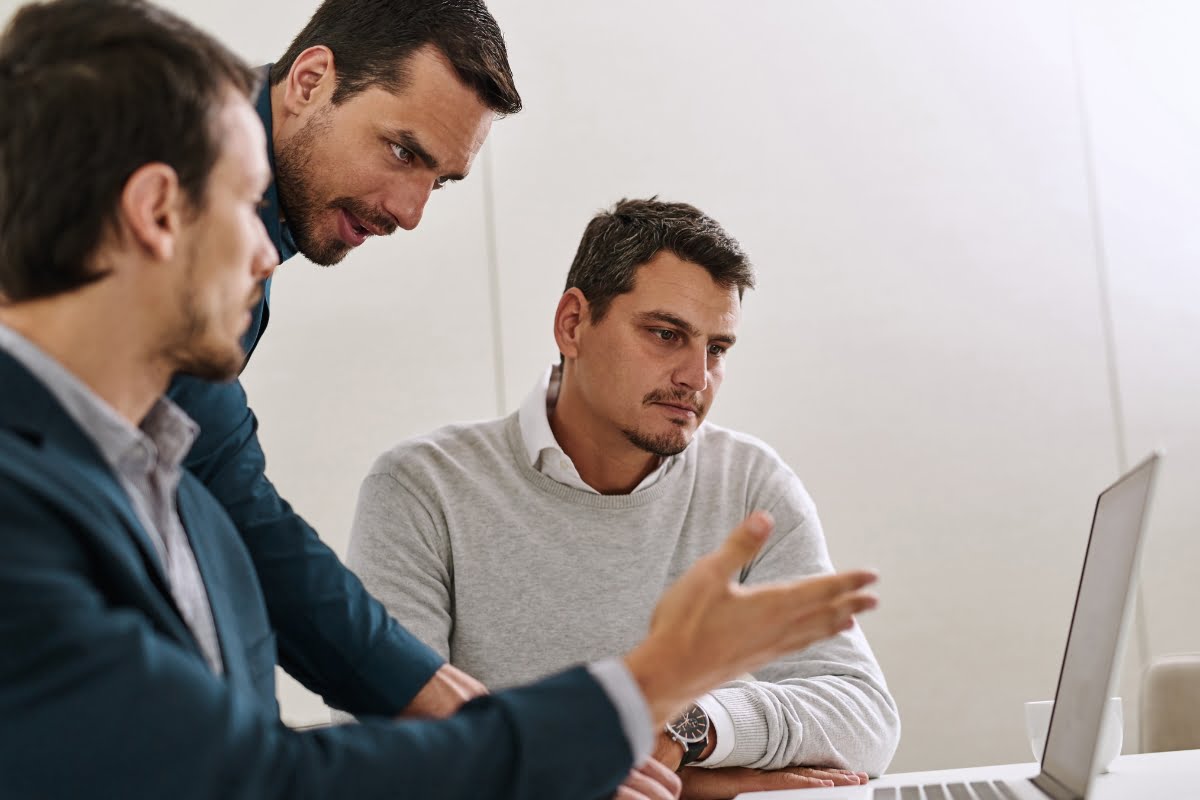 Three businessmen fixing a laptop in an office.