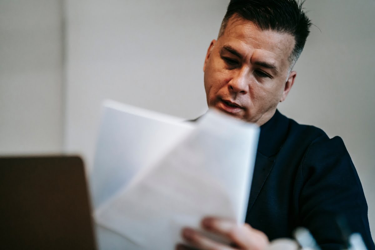 A man fixing a suspended business profile while looking at a piece of paper in front of a laptop.