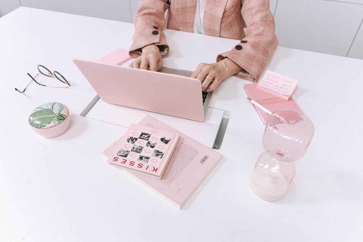 A woman fixing suspended business profiles at a desk with a pink laptop.