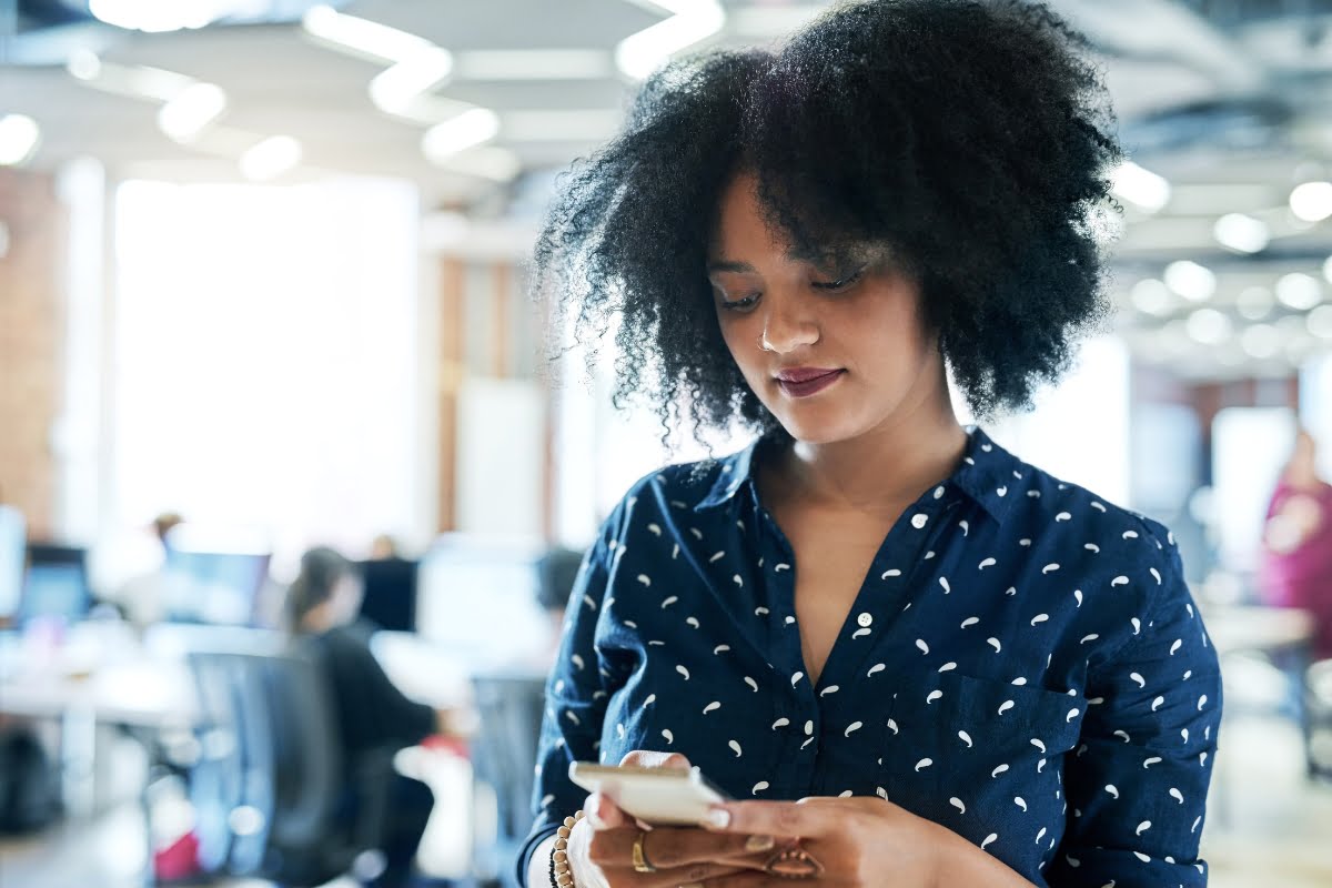 A young woman fixatedly looking at her phone in an office, troubleshooting suspended business profiles.