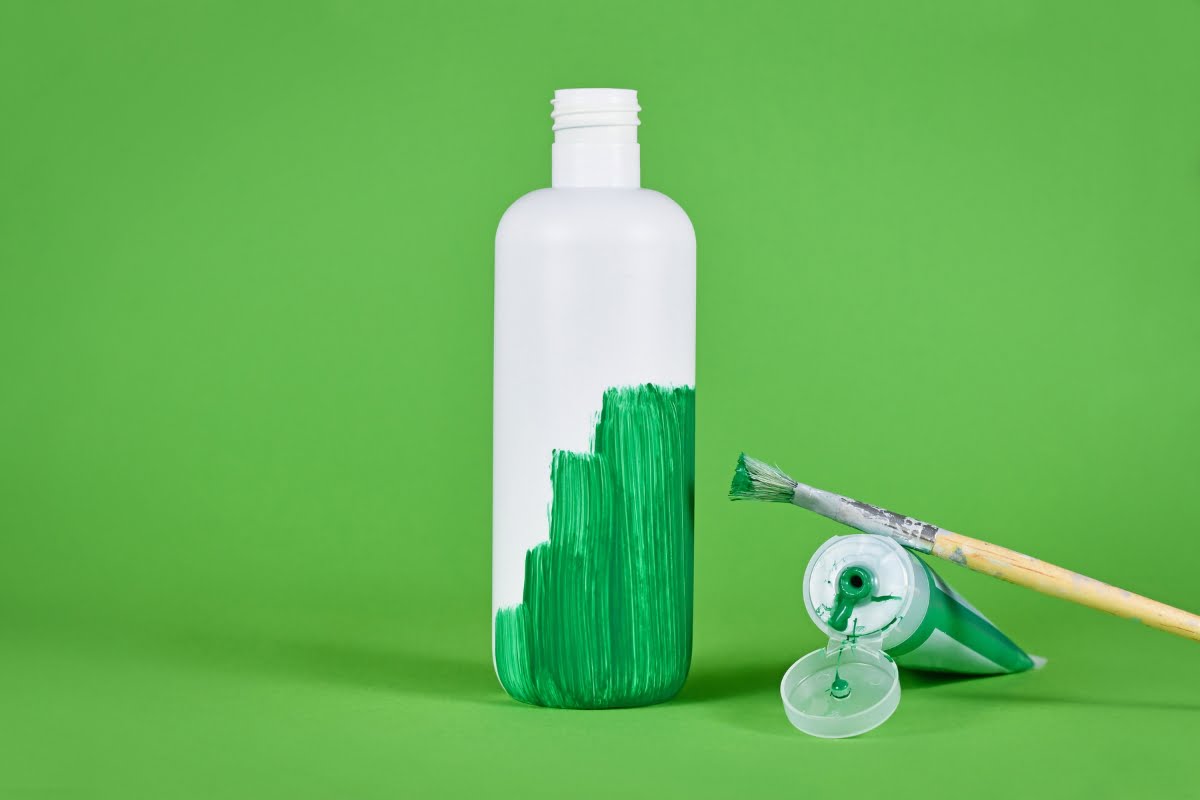 A green paint bottle and brush on a green background, demonstrating eco-friendly color application techniques.