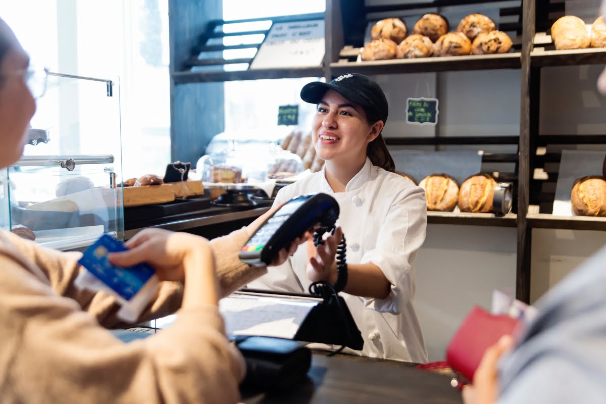 A woman is paying for a loaf of bread at a local bakery.