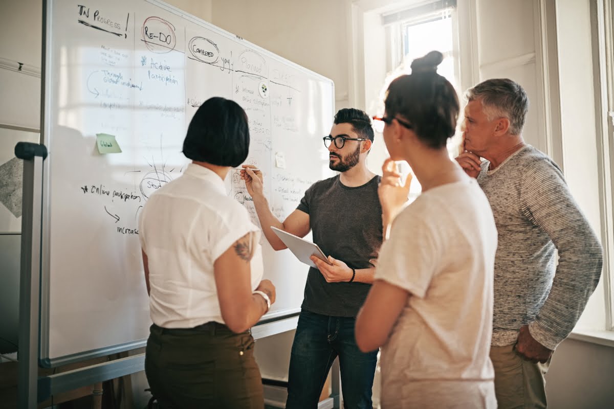 A boutique agency of people standing around a whiteboard.