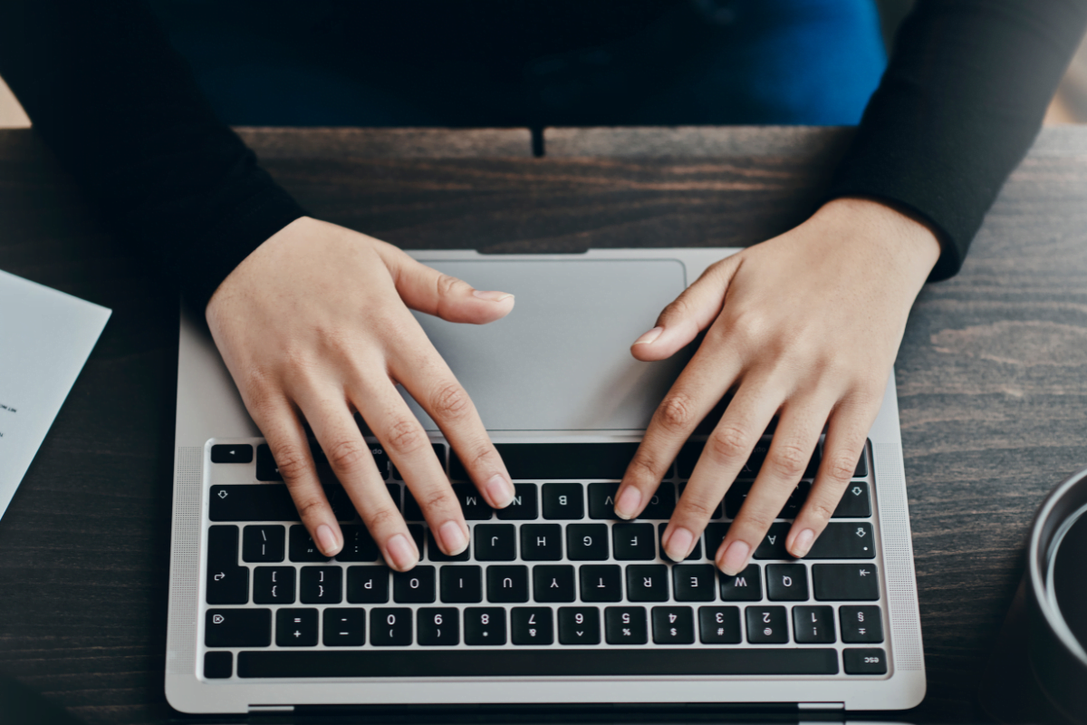 A woman typing on a laptop while enjoying a cup of coffee, using her device to seamlessly embed PDFs.