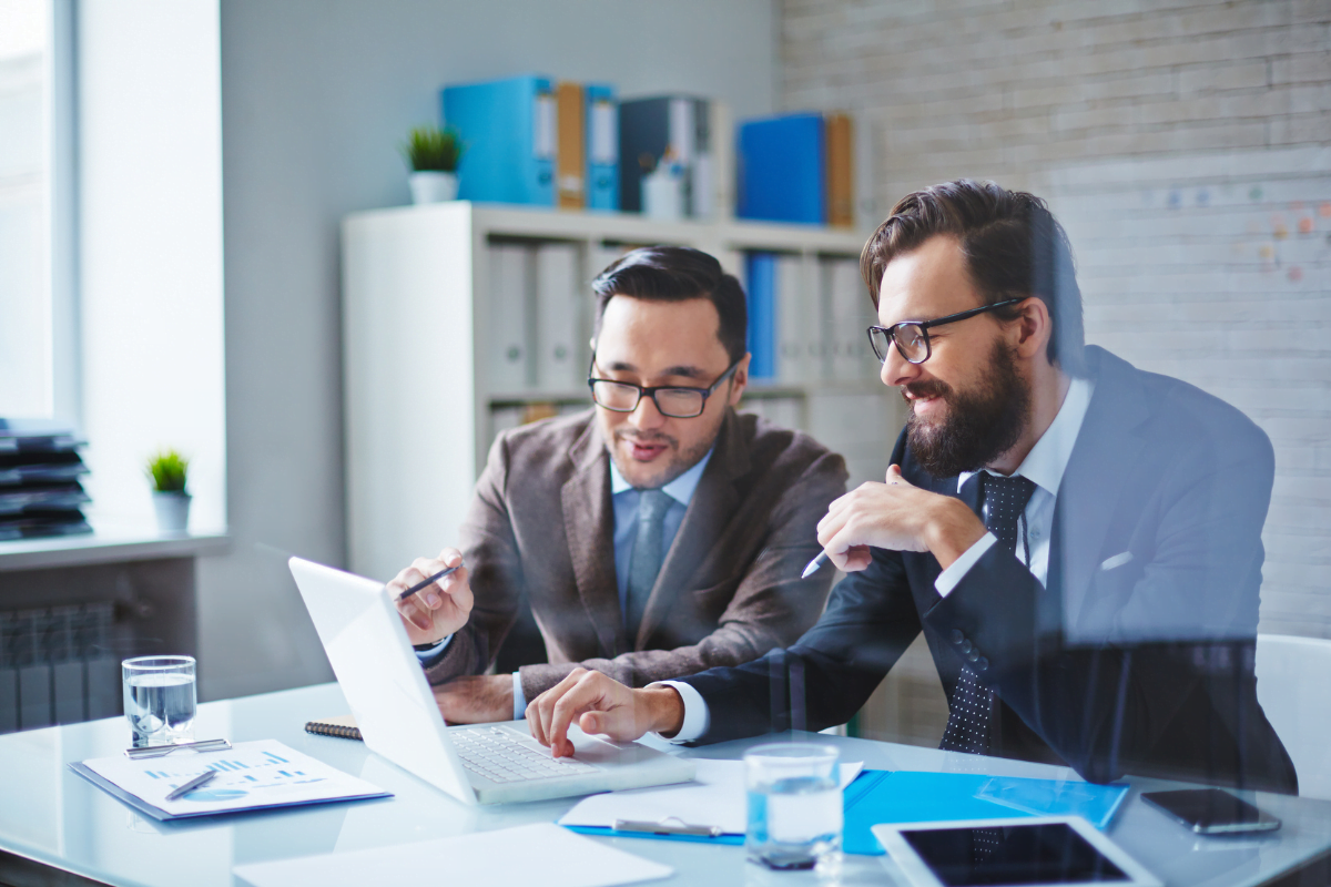 Two businessmen hiring an SEO consultant, looking at a laptop in an office.