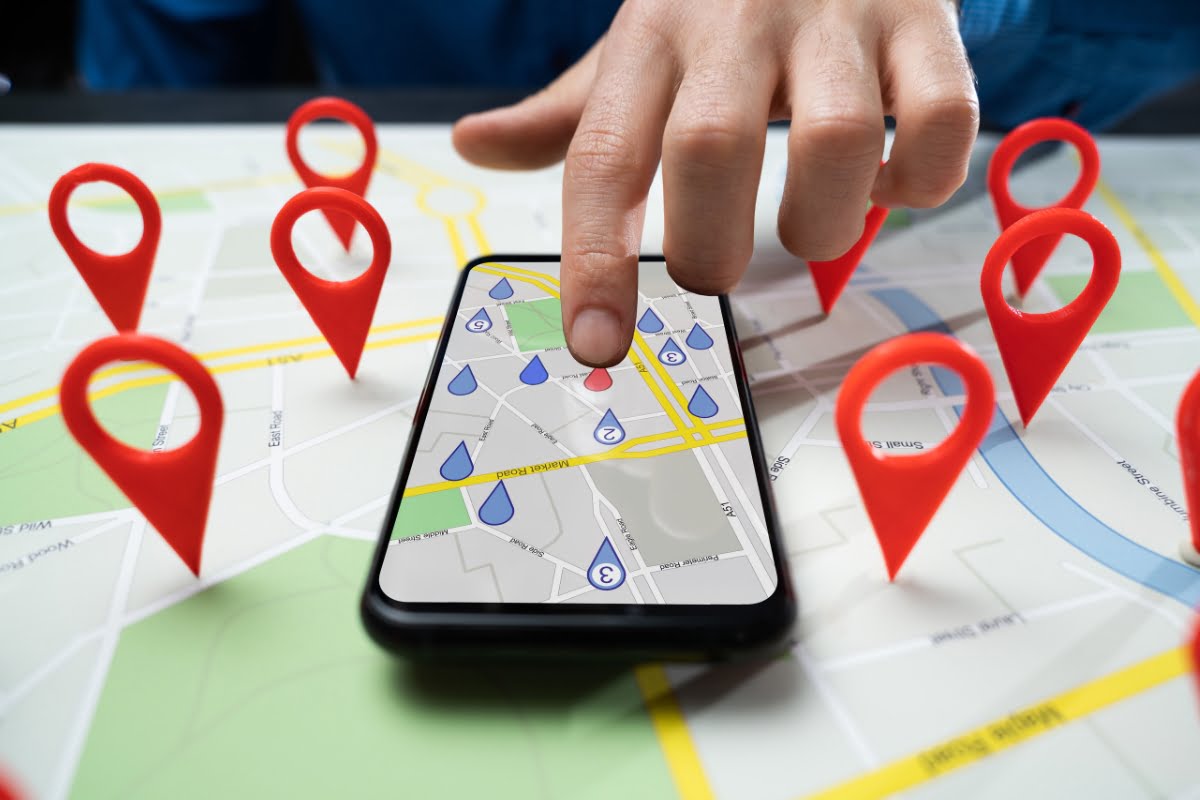 A person holding a smartphone with pins on a map while managing a home improvement business.