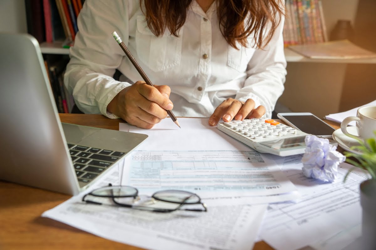 A woman is working on her taxes at a desk with a calculator in the comfort of her home.