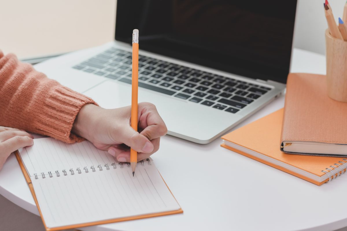 A woman's hand meticulously writing on a notebook with a pencil, researching and taking notes on ways to increase domain authority.