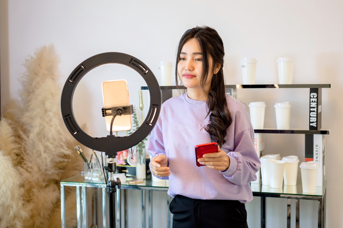 An influencer executing an Instagram marketing strategy, holding a cell phone in front of a ring light.