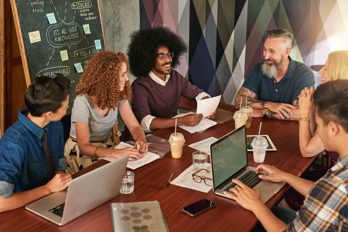 A group of people sitting around a table discussing their Instagram marketing strategy, each engrossed in their laptops.