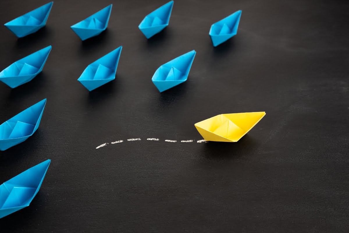 A cluster of paper boats featuring a standout yellow vessel in the center.