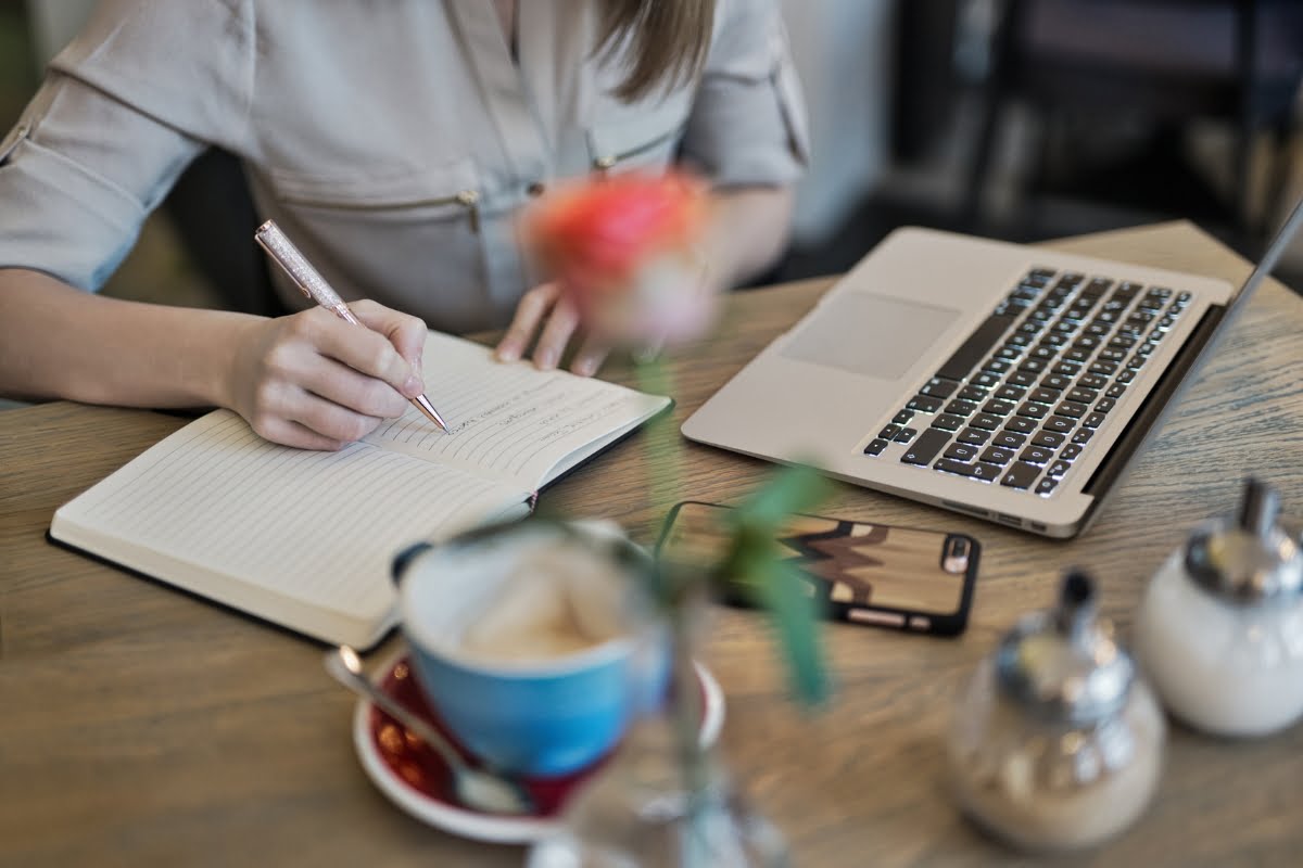 A woman writing in a notebook at a table with a laptop, focused on landing page conversions.