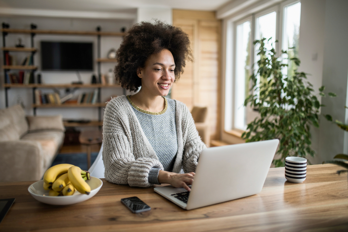 A woman sitting at a table with a laptop and bananas nearby.