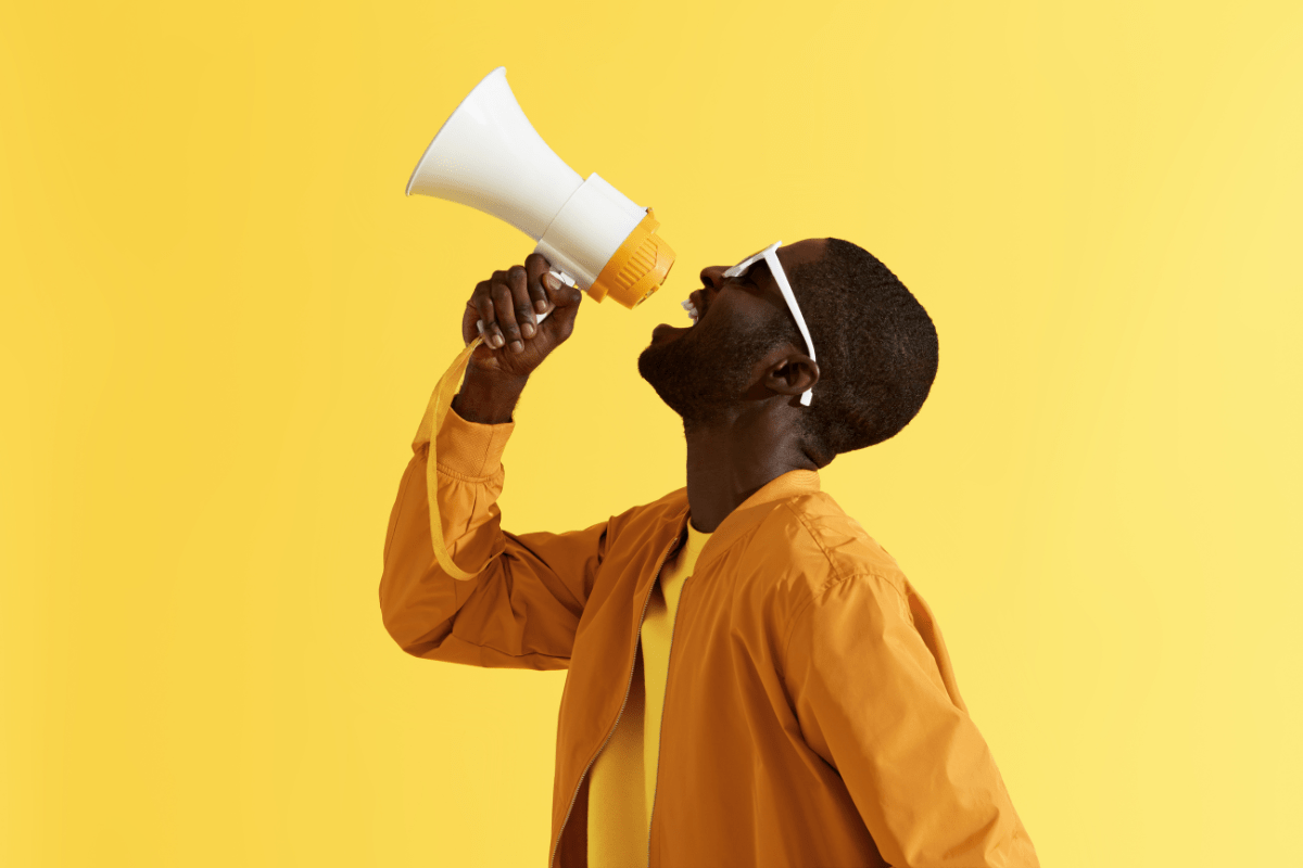 A man passionately marketing his message through a megaphone against a vibrant yellow background.