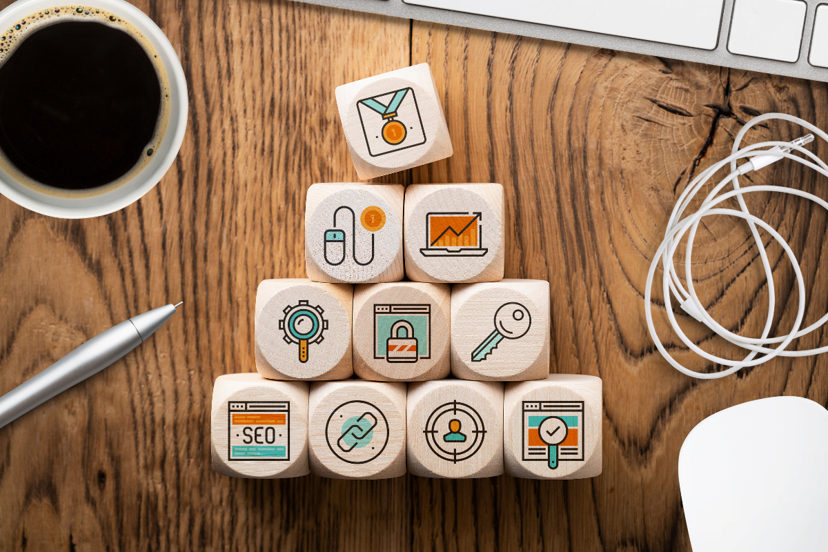 A wooden block with icons on it next to a computer and a cup of coffee, showcasing marketing strategies for remodeling contractors.