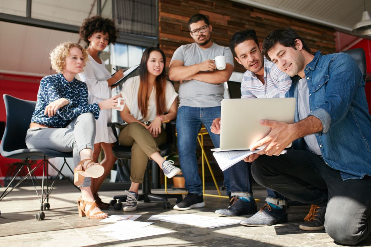 A group of people brainstorming marketing strategies for startups while sitting around a laptop.