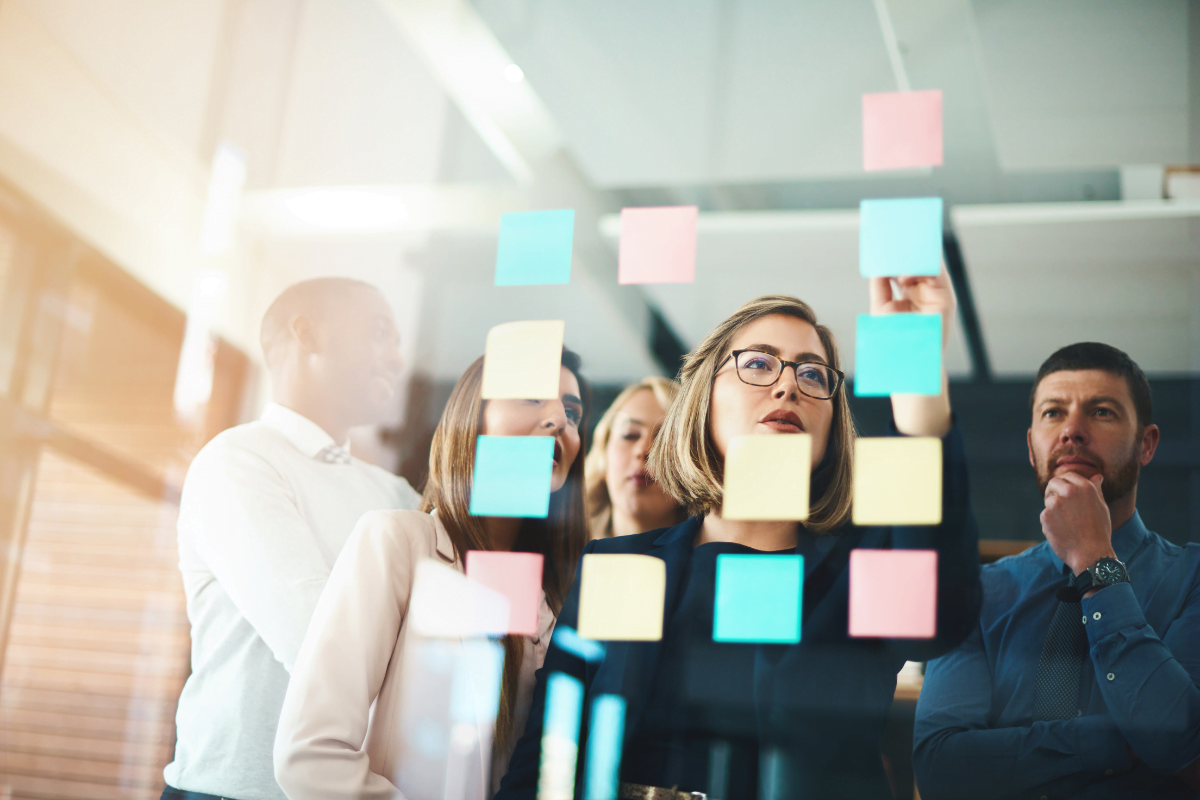 A group of people performing SEO competitor analysis, examining sticky notes on a glass wall.