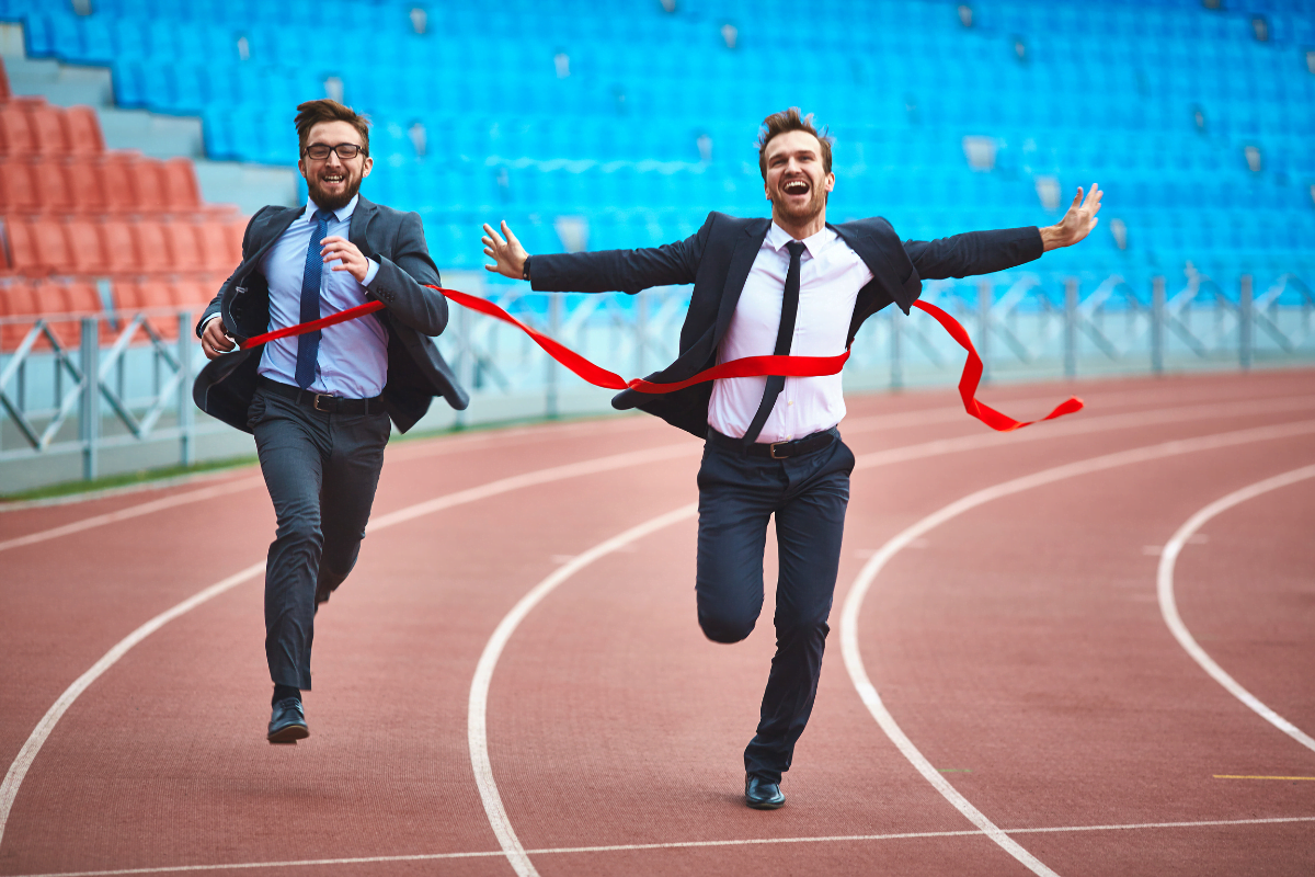 Two businessmen competing in a race on a track in a stadium.