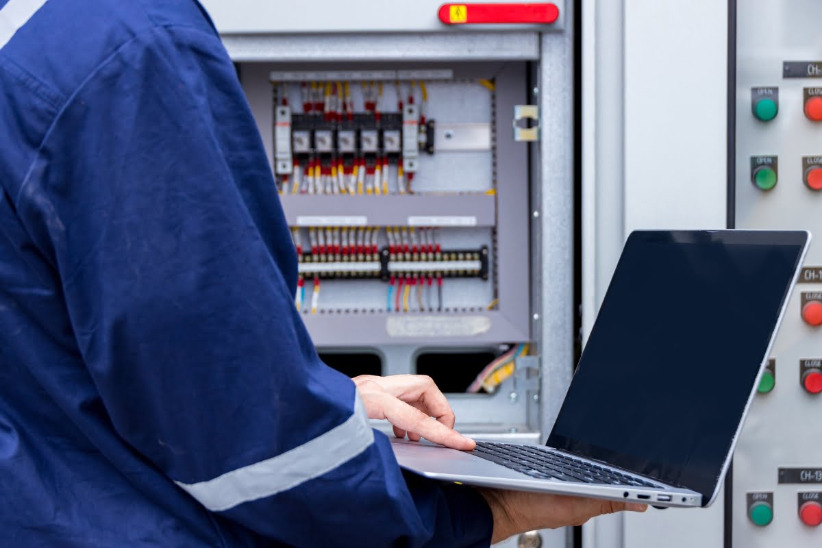 A man is using a laptop to perform SEO for electricians in front of an electrical panel.