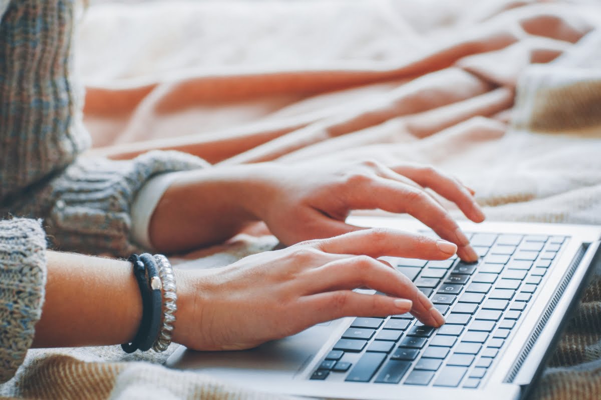 A woman implementing SEO strategies on a laptop for digital marketing while sitting on a bed.