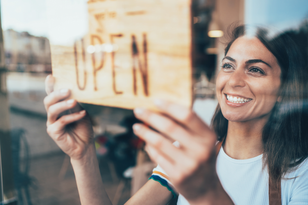 A woman holding up a sign that says open for a small business.