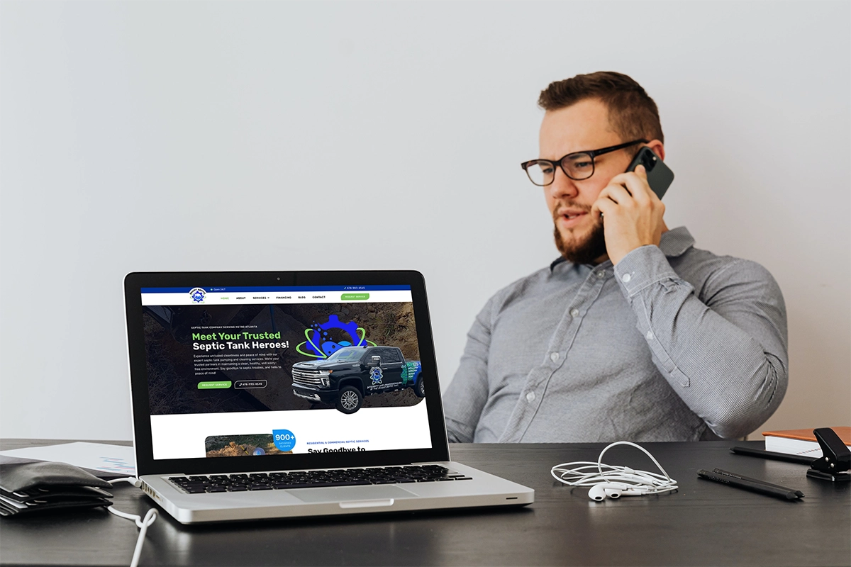 A man is talking on the phone while sitting at a desk with a laptop. There is no relevance or connection to the keywords "septic" and "Smart Septic Pros" in this description.