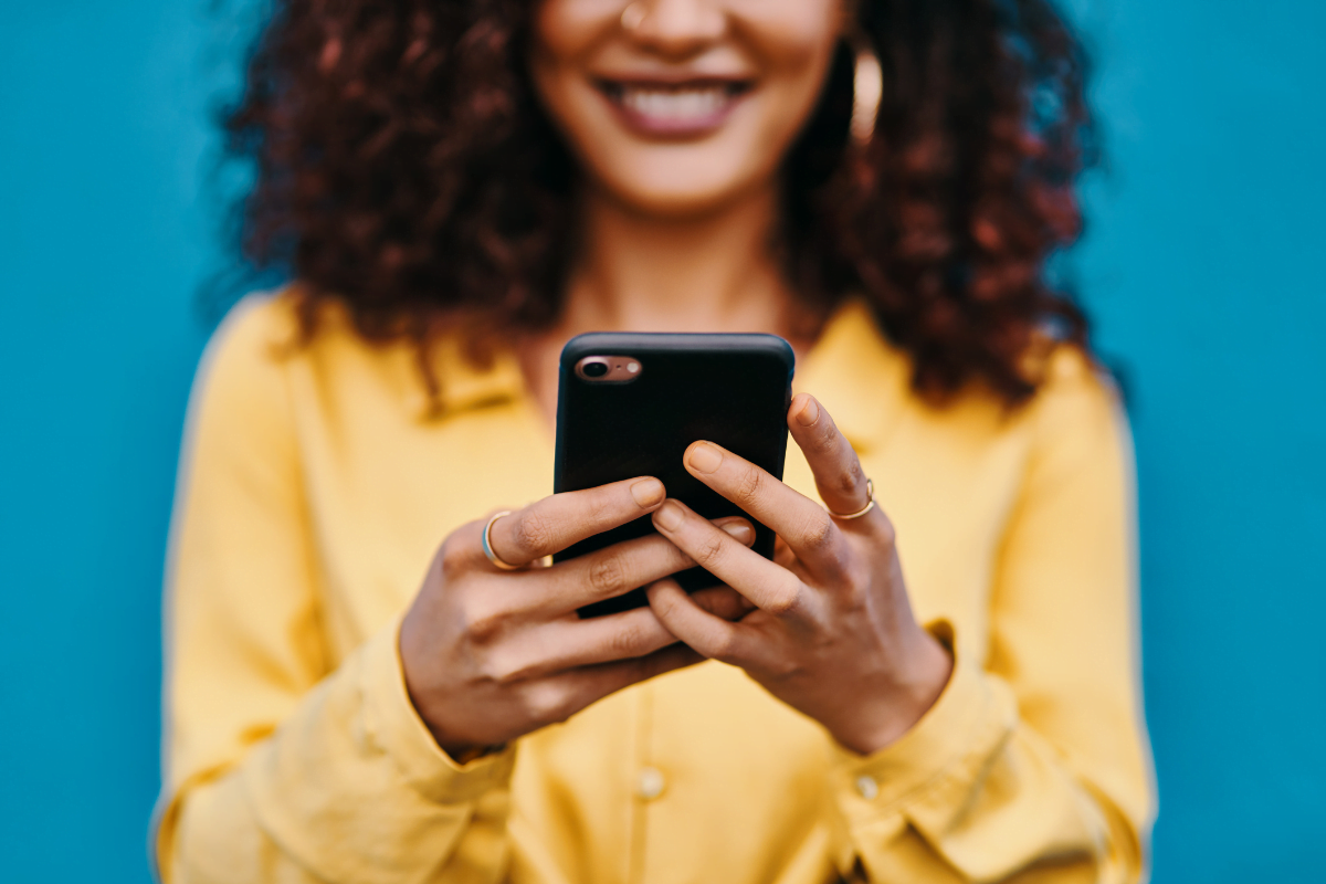 A woman with curly hair is happily using a cell phone.