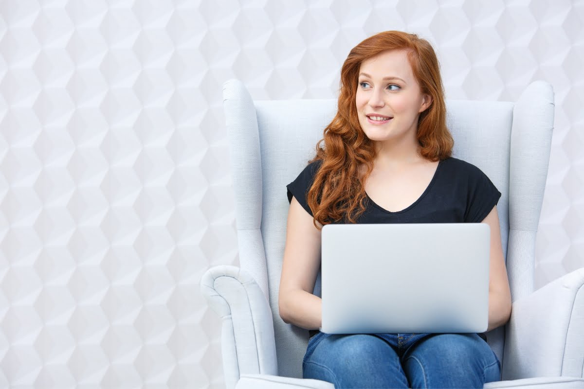 A young woman writing copy sitting in a chair with a laptop.